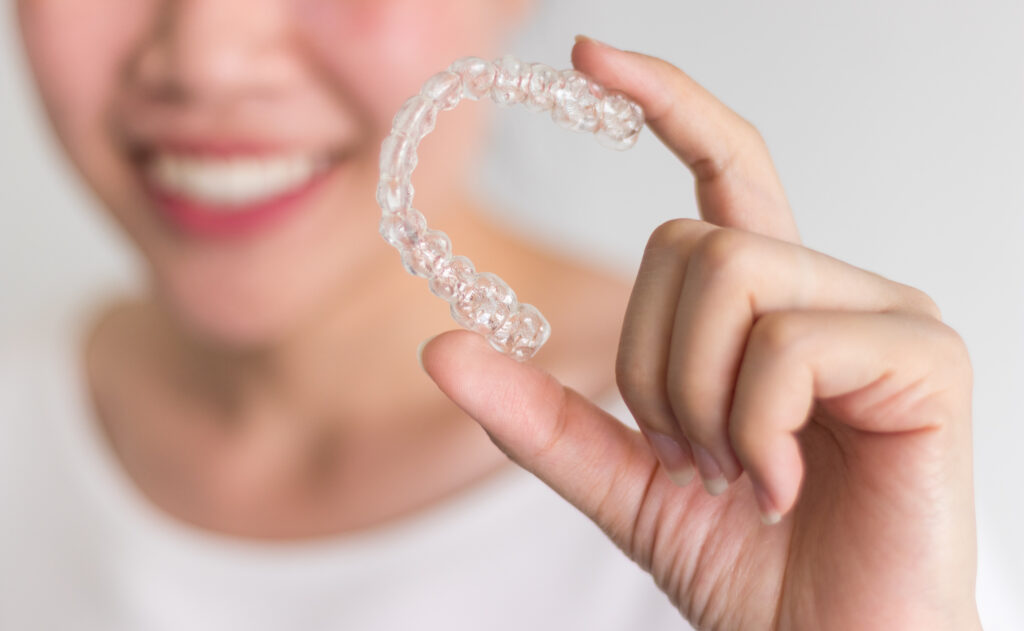 A smiling woman holding invisalign