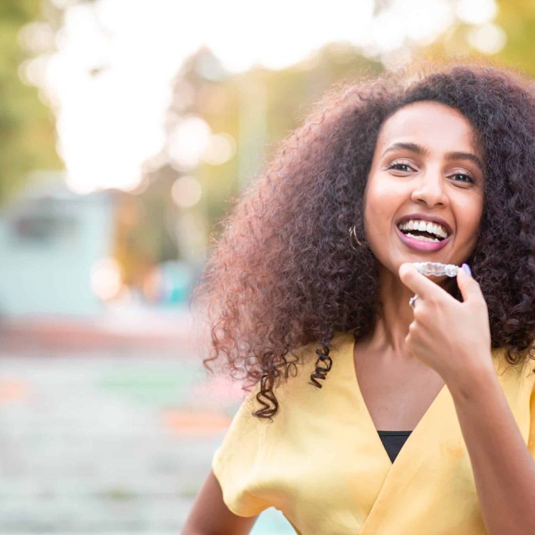 Beautiful smiling African black woman is holding invisaligner. Includes copy and text space.