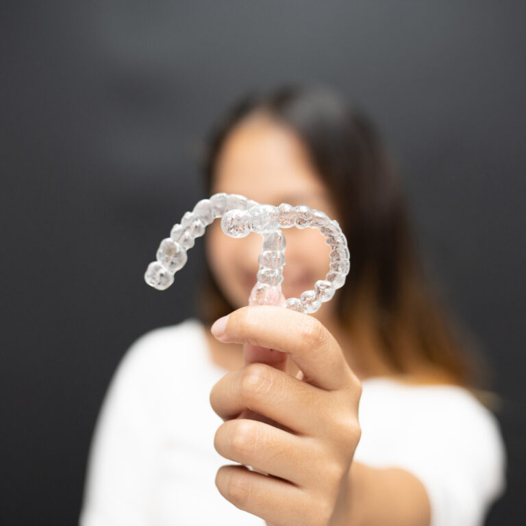 Women hand hold inivisalign braces, transparent aligner, invisible retainer or orthodontic silicone trainer with blur mile in background. A way to have a beautiful smile.
