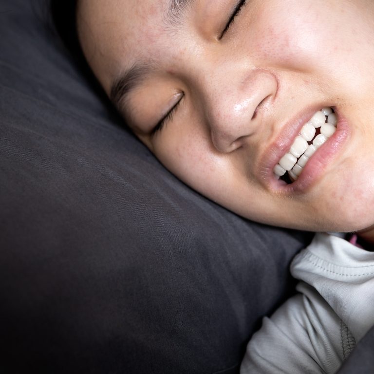 Asian child girl suffering from bruxism while lying in bed at night,female grinding of the teeth during sleep,teeth clenching,sleep disorders,oral health problems,dental care medical,bruxism concept