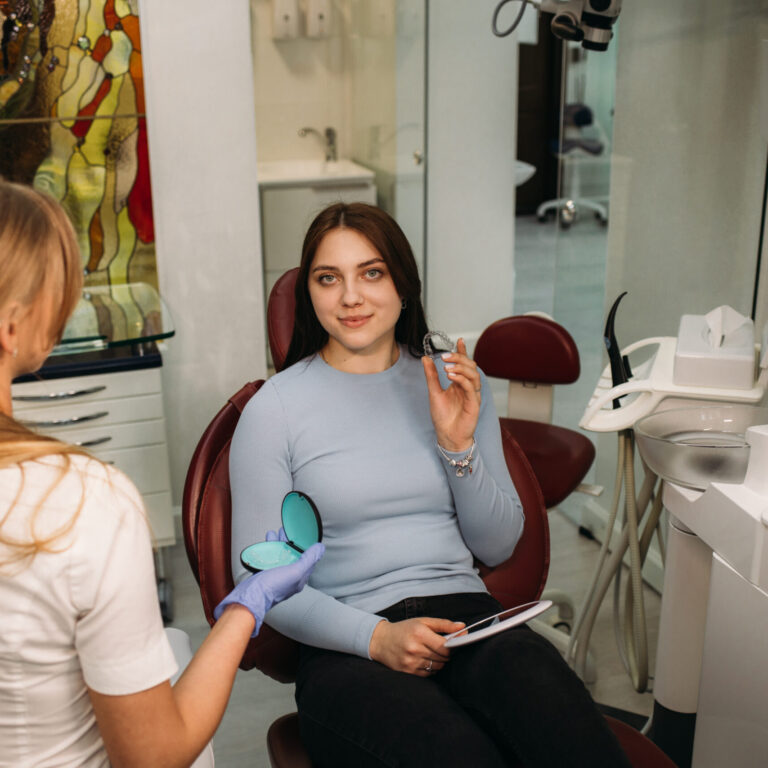 woman holds aligners in dentistry while sitting in dental chair.