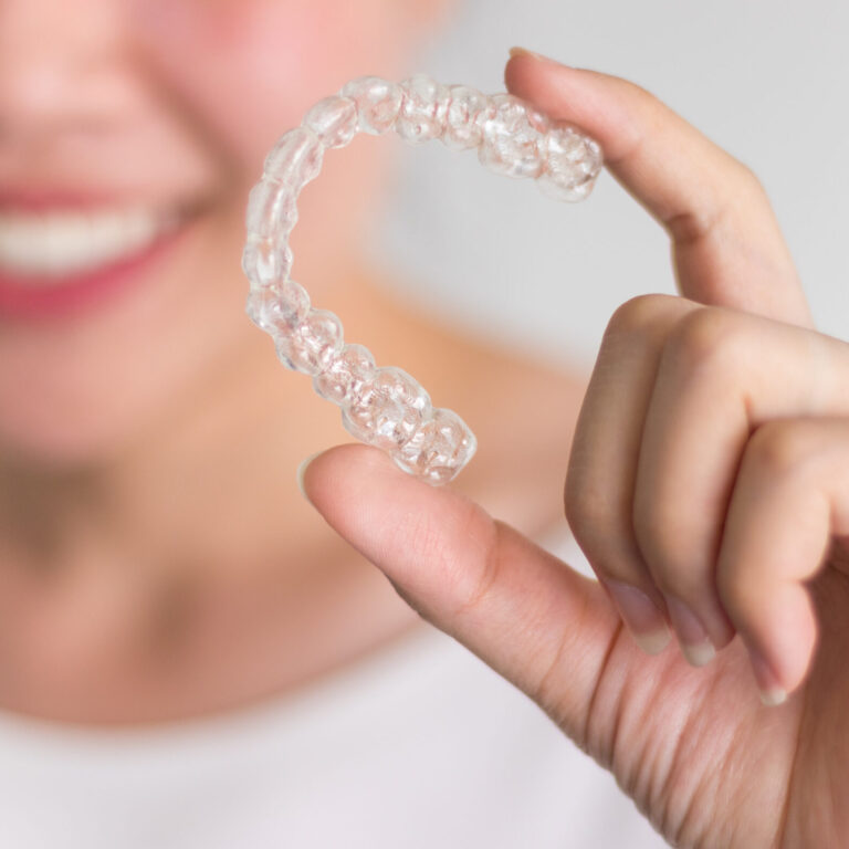 A smiling woman holding invisalign