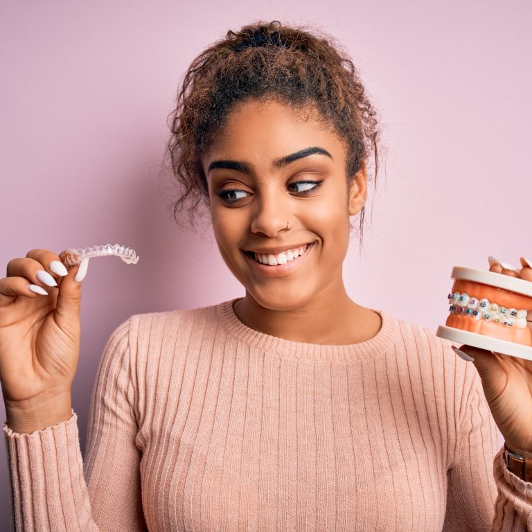 Young african american woman smiling happy holding professional orthodontic denture with metal braces and removable invisible aligner. Comparation of two dental straighten treatments